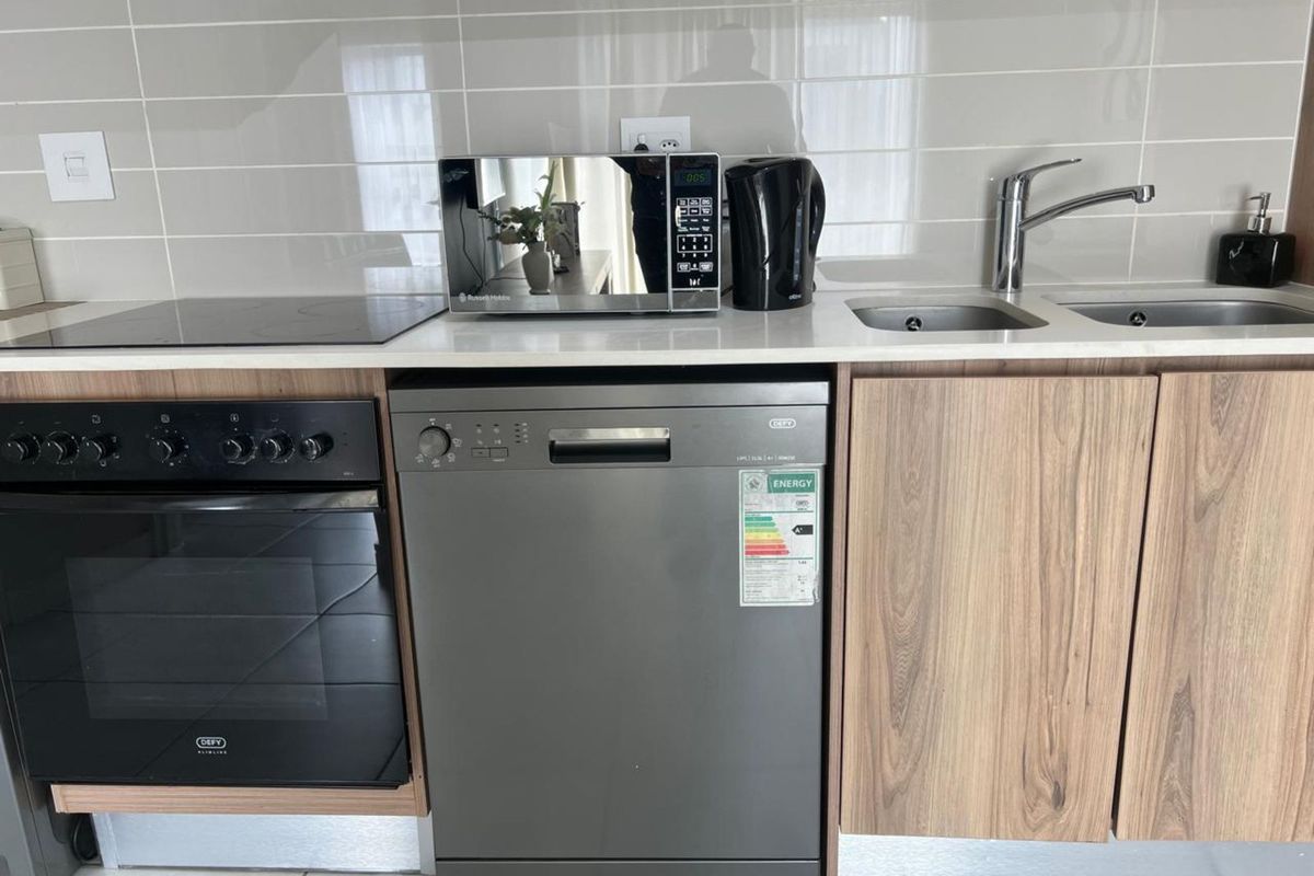 Modern kitchen featuring a built-in oven, induction hob, double sink with mixer tap, and integrated dishwasher with wood-finish cabinetry and tiled backsplash.