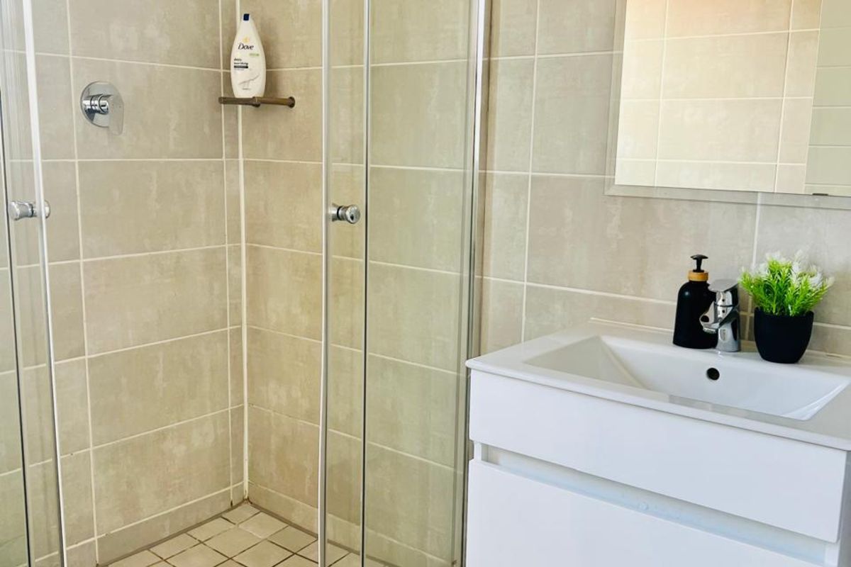 A modern bathroom featuring a glass-enclosed shower with neutral wall tiles and a contemporary wall-mounted vanity unit with a basin.