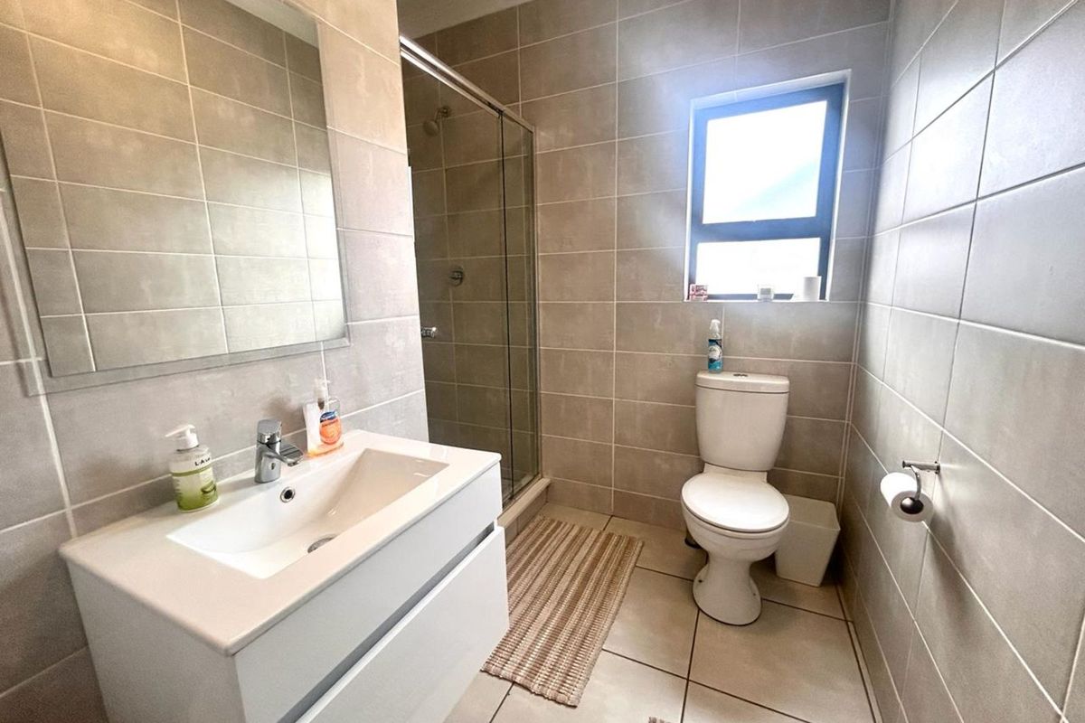 Modern bathroom featuring floor-to-ceiling neutral tiling, a glass-enclosed shower, a wall-mounted vanity with basin, and a toilet.