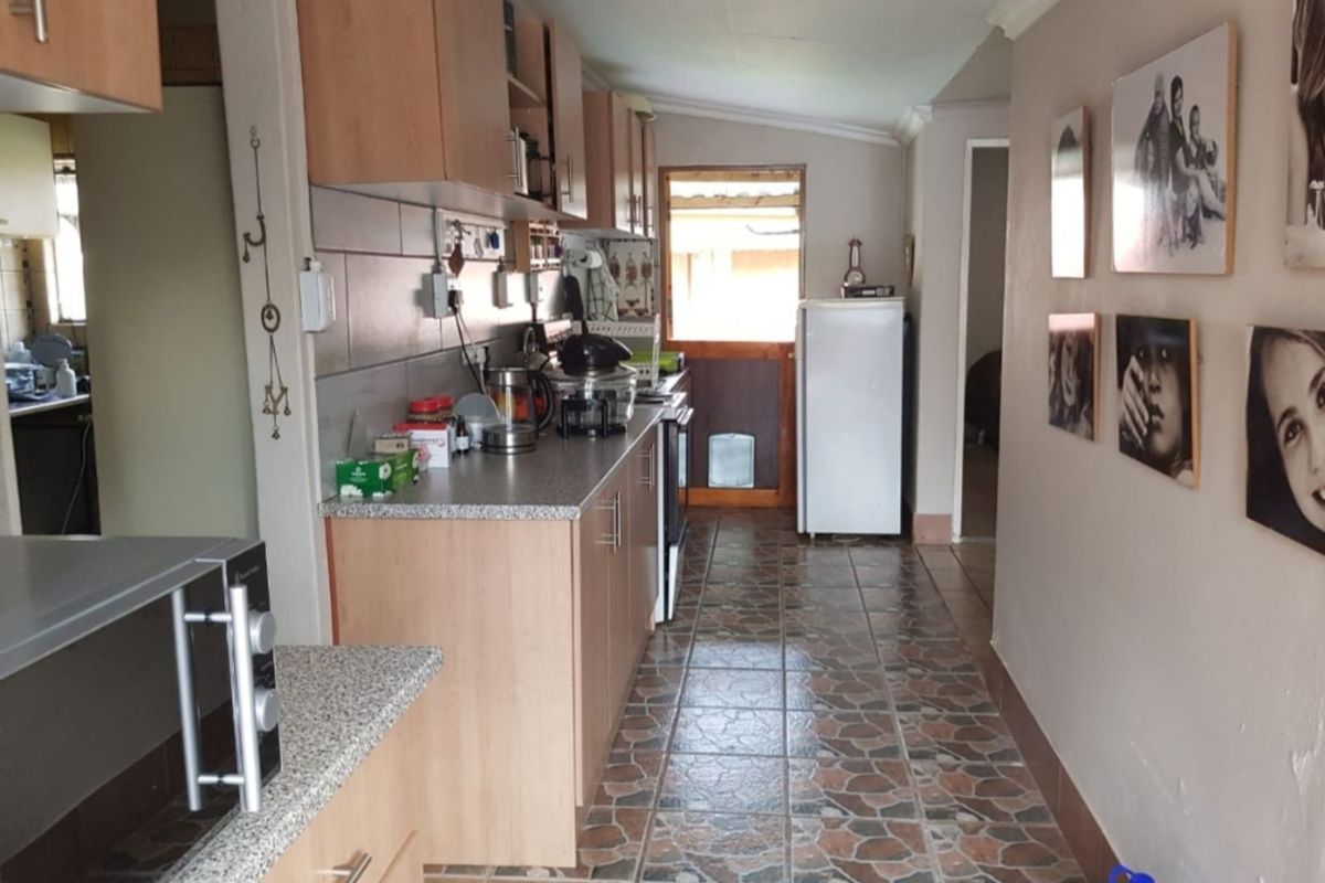 A functional galley-style kitchen featuring laminate cabinetry, stone-look countertops, and tiled flooring, leading to an exterior door.