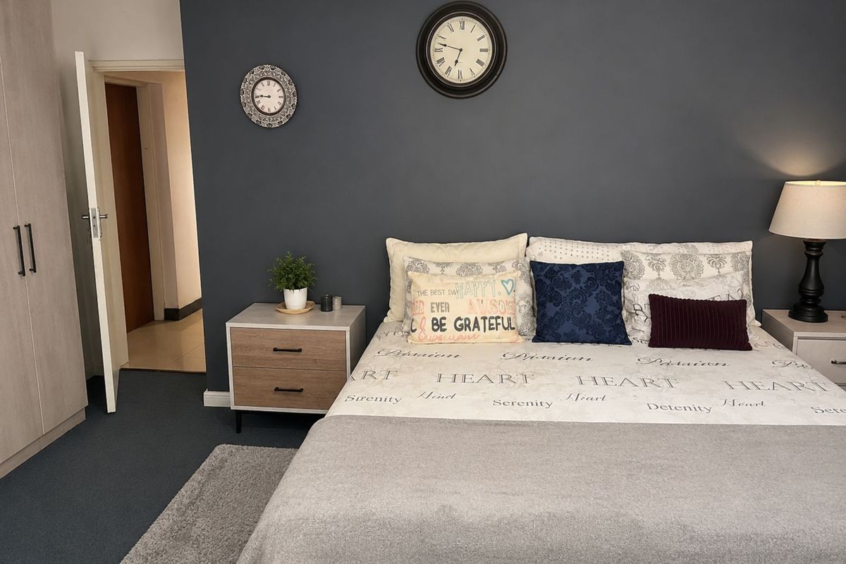 A well-maintained bedroom featuring a dark accent wall, built-in wardrobe storage, and neutral carpeting.