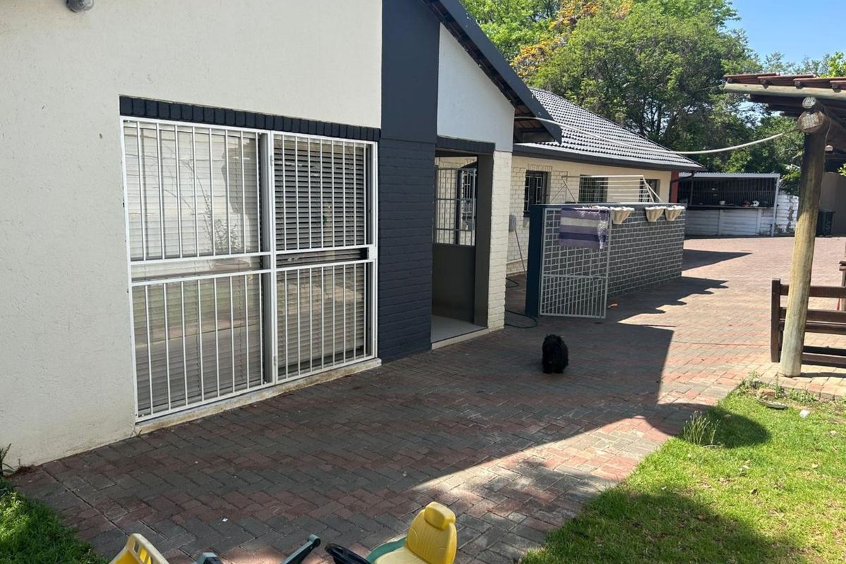 Rear exterior view of the property featuring a paved patio area, security bars on windows, and a brick boundary wall.