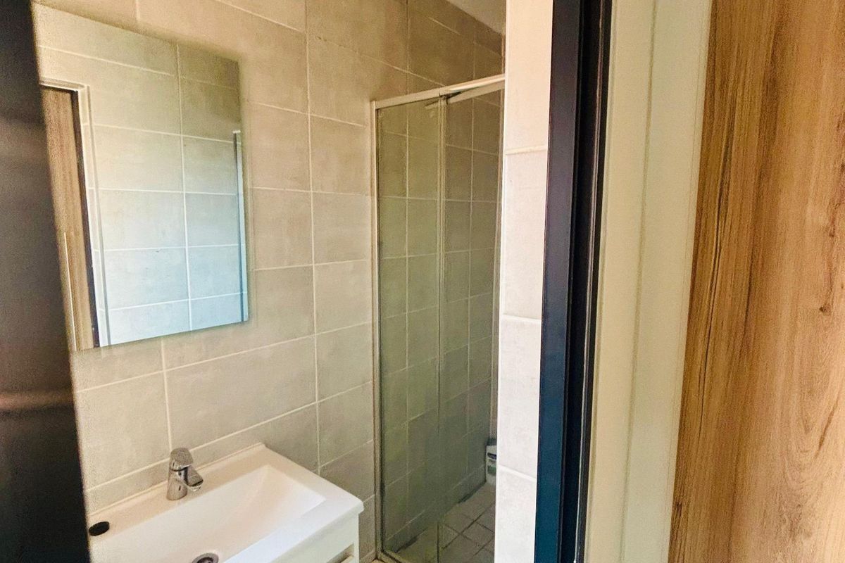 A modern bathroom featuring a wall-mounted vanity with basin, a frameless mirror, and a glass-enclosed shower with neutral wall tiling.