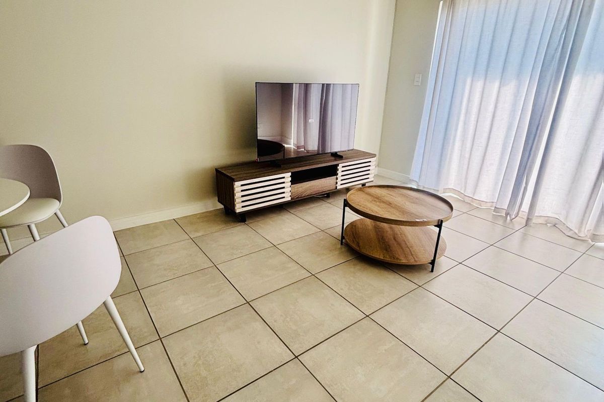 A bright living area featuring neutral ceramic floor tiles and large sliding glass doors with curtains, providing access to the exterior.