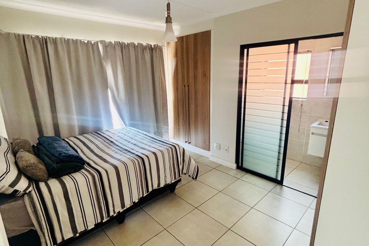 A bedroom featuring tiled flooring, built-in wooden cupboards, and an en-suite bathroom accessed through a sliding glass door.