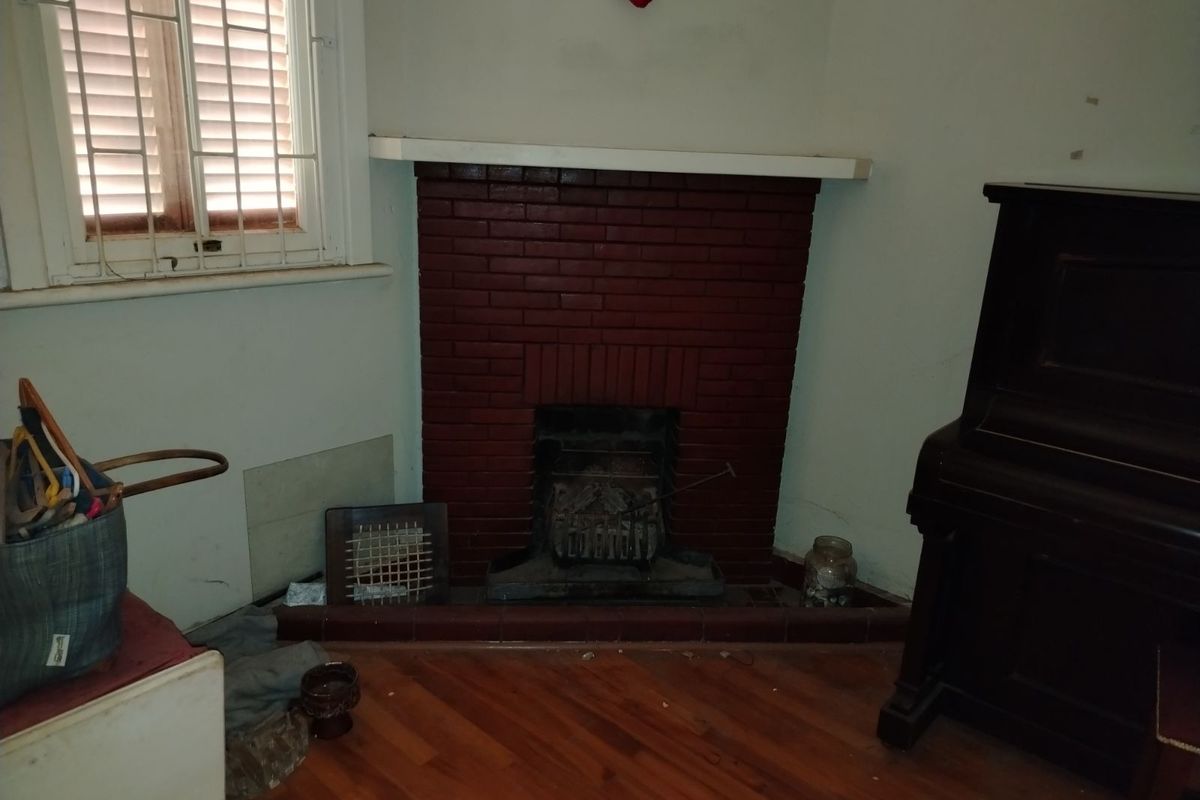 A living room featuring a traditional red brick fireplace with a mantelpiece and timber flooring, offering a classic architectural foundation for renovation.