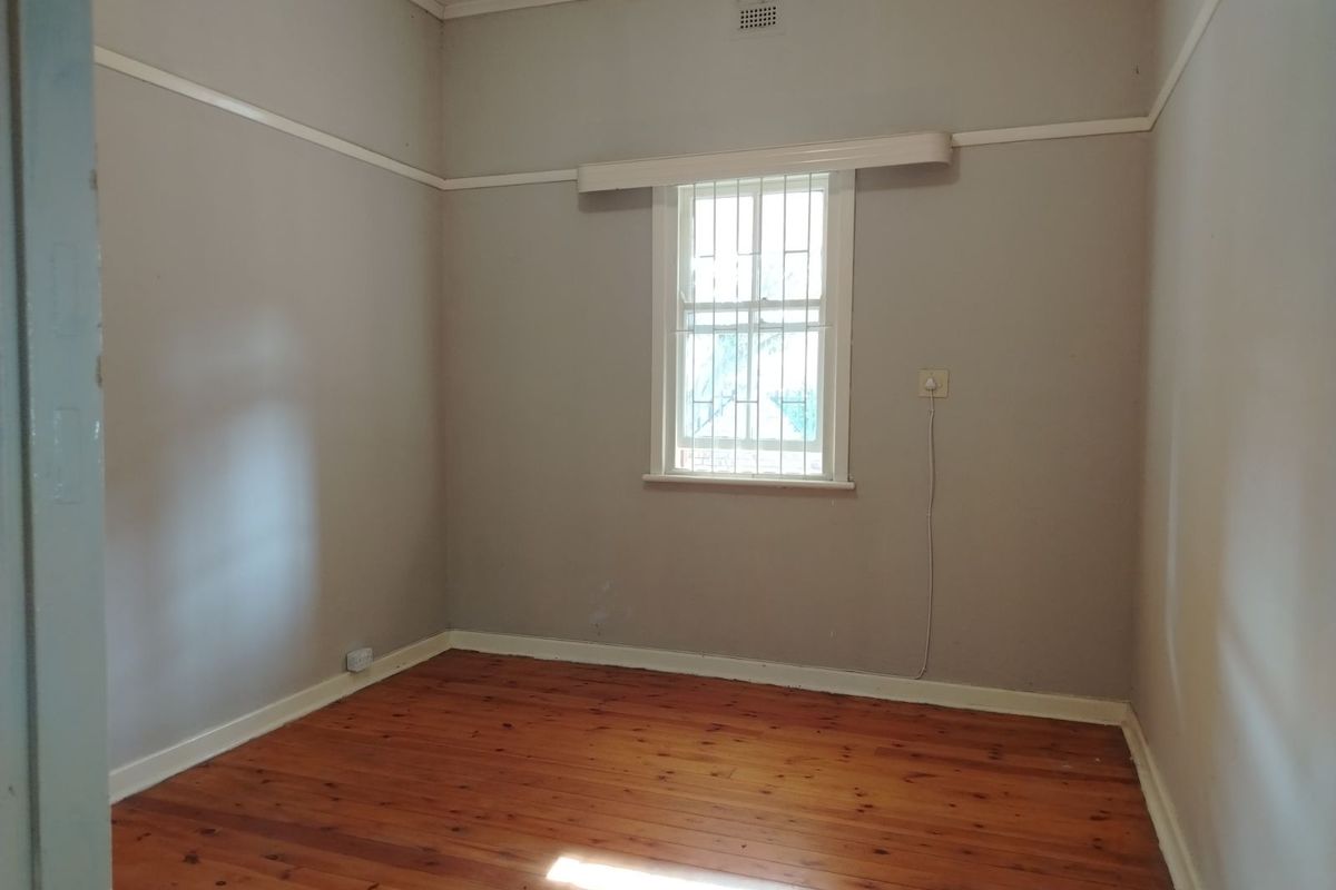 A vacant bedroom featuring polished timber flooring, neutral wall tones, and a window fitted with security bars.