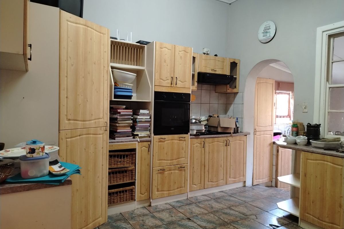 A functional kitchen featuring light wood cabinetry, built-in oven, extractor fan, and tiled flooring, with an arched doorway leading to an adjacent space.