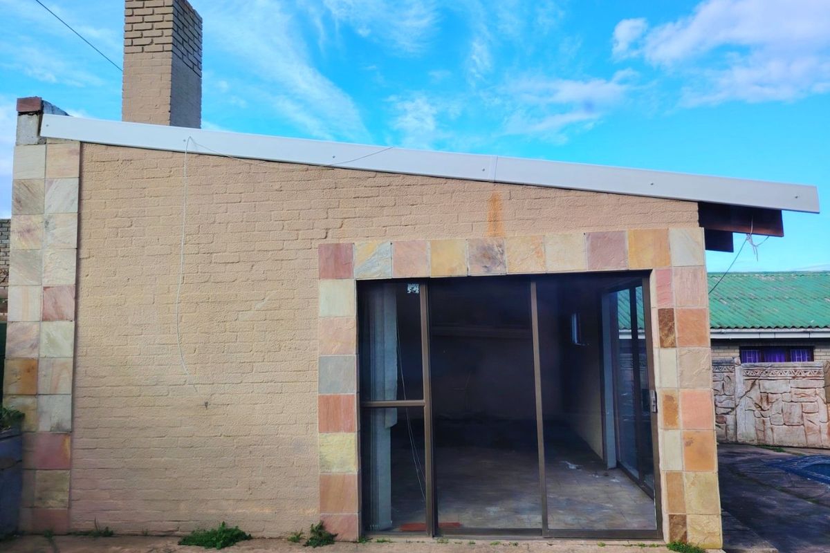 Rear exterior view of a house featuring a brick chimney, sliding glass doors, and decorative stone tile accents around the entrance.