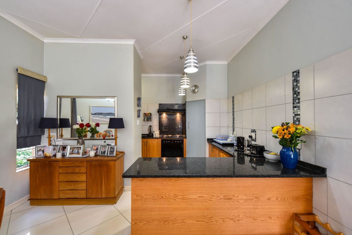 A functional kitchen featuring wooden cabinetry, dark granite countertops, a built-in oven and hob, and a breakfast bar island.