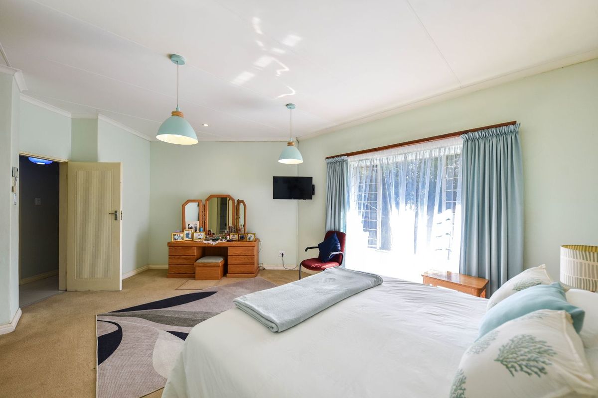 Spacious bedroom featuring large windows with curtains, neutral wall tones, and pendant lighting, offering a comfortable and functional living space.