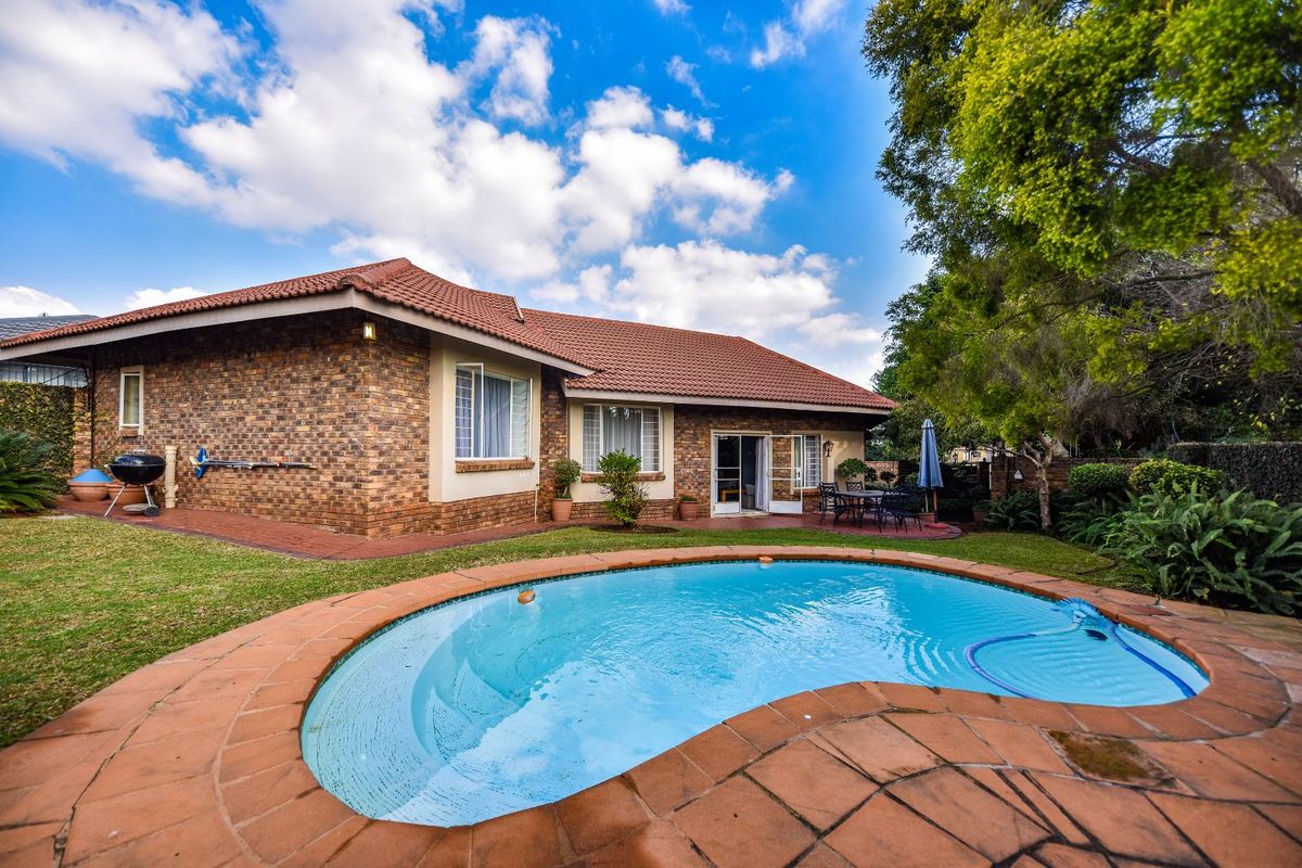 Rear view of a brick house featuring a swimming pool, paved patio area, and established garden surroundings.