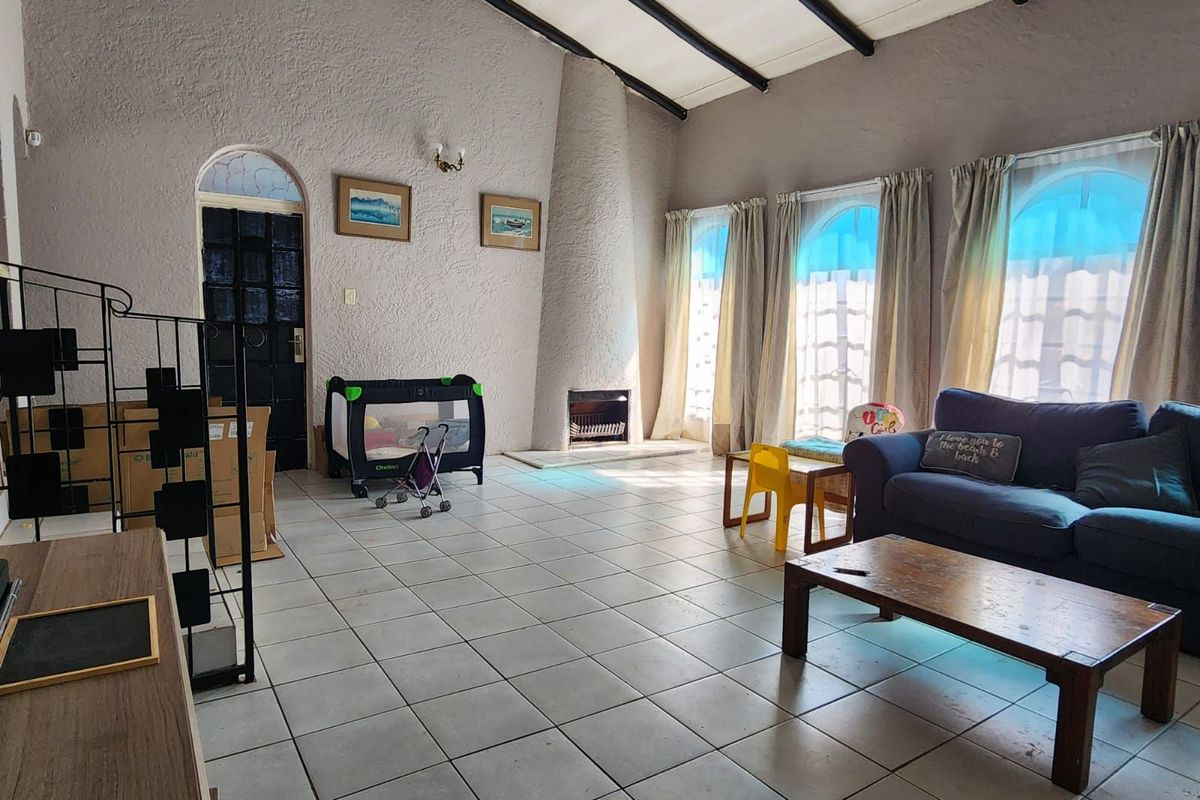 Spacious living room featuring high vaulted ceilings with exposed beams, a built-in fireplace, and large arched windows allowing for ample natural light.