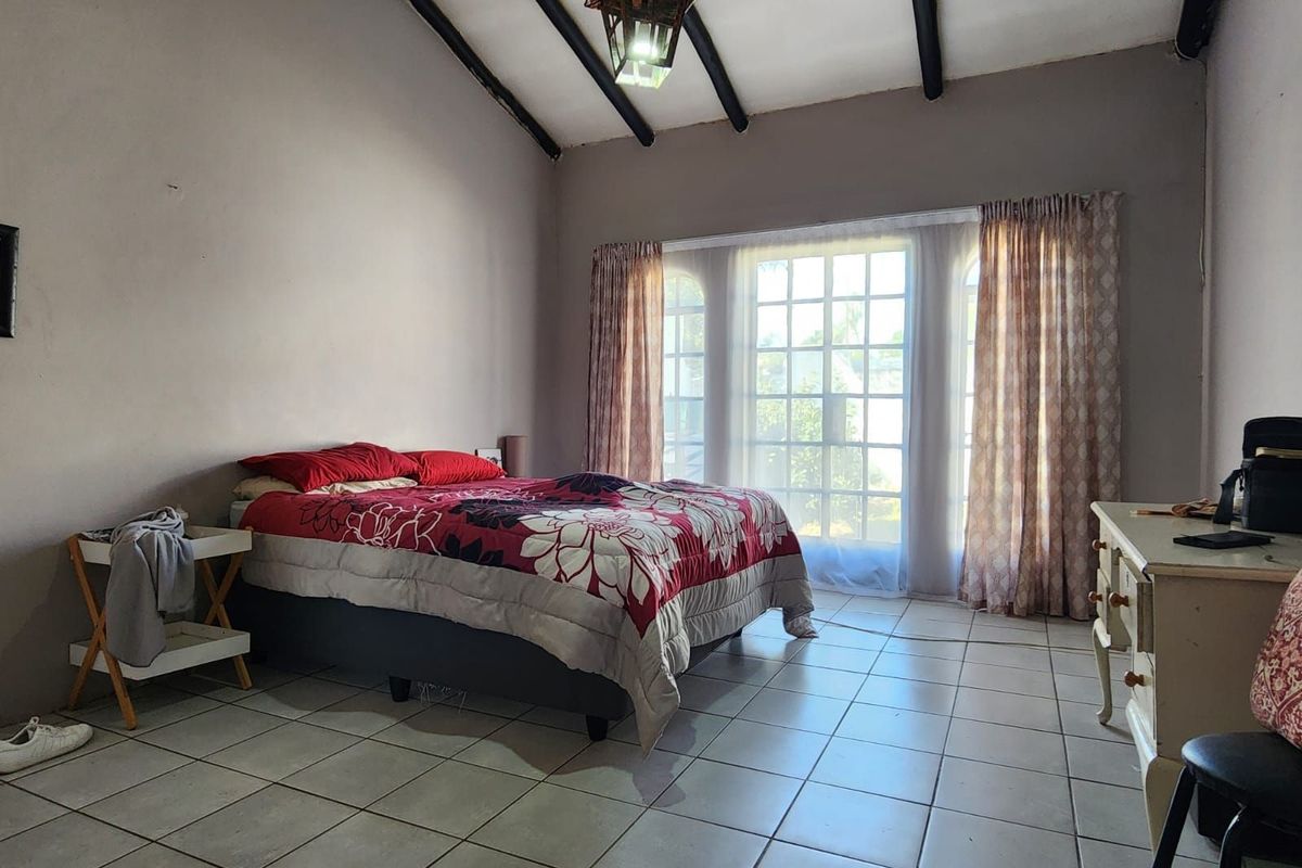 Spacious bedroom featuring vaulted ceilings with exposed timber beams, tiled flooring, and large glass-paned doors providing natural light.