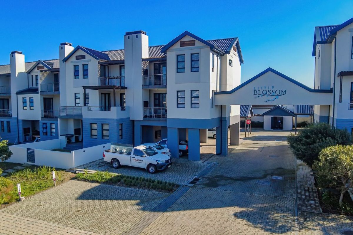 Aerial view of the Little Blossom apartment complex, showcasing the multi-story residential buildings, paved driveway, and covered entrance archway.