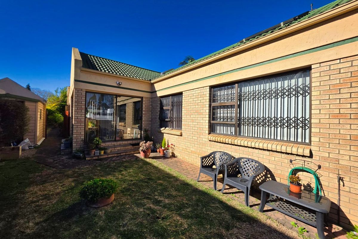 Rear view of the house featuring a brick facade, tiled roof, and a paved patio area with security gates on the windows.