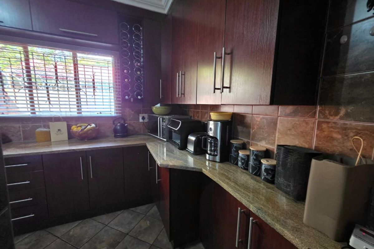 A functional kitchen featuring dark wood cabinetry, granite countertops, tiled backsplash, and tiled flooring with a window providing natural light.