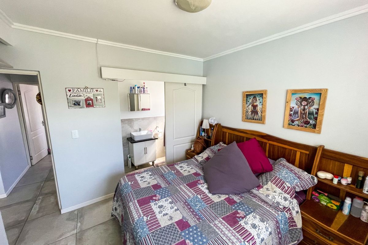 A bedroom featuring tiled flooring and an adjoining en-suite bathroom area with a vanity and sliding door access.