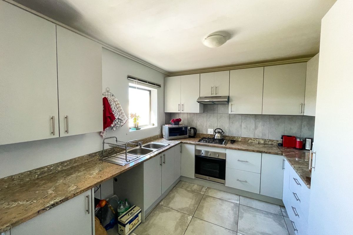 A functional kitchen featuring light-toned cabinetry, granite countertops, tiled flooring, and built-in appliances including an oven, hob, and extractor fan.