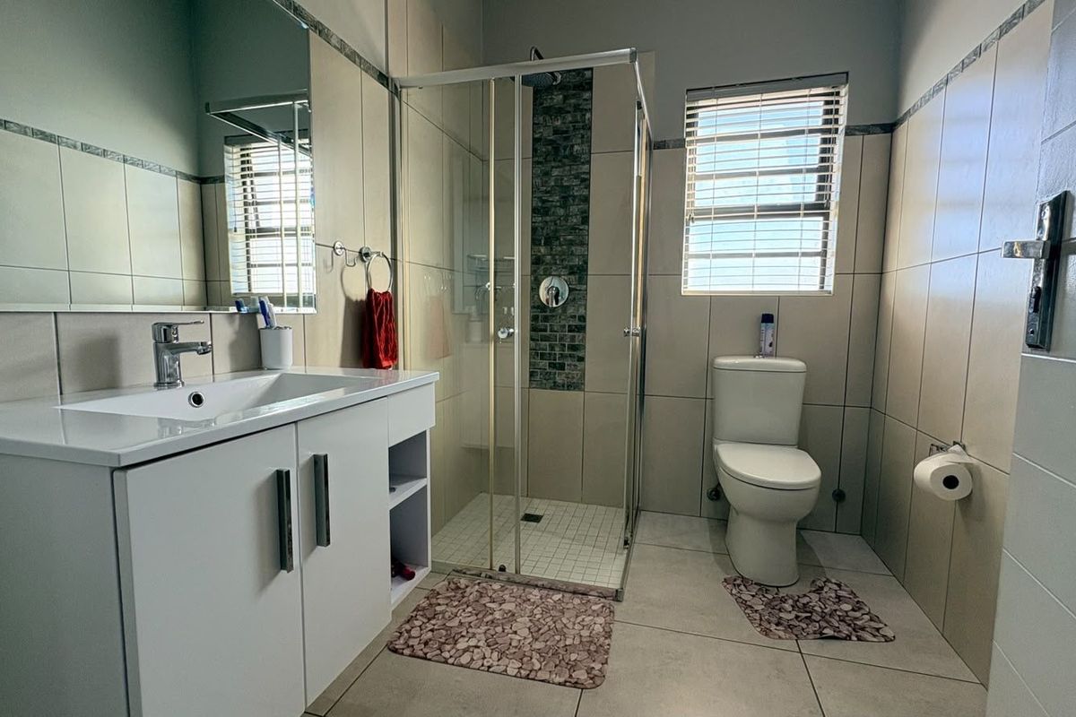A well-maintained bathroom featuring a glass-enclosed shower, modern vanity with integrated basin, and neutral wall tiling.