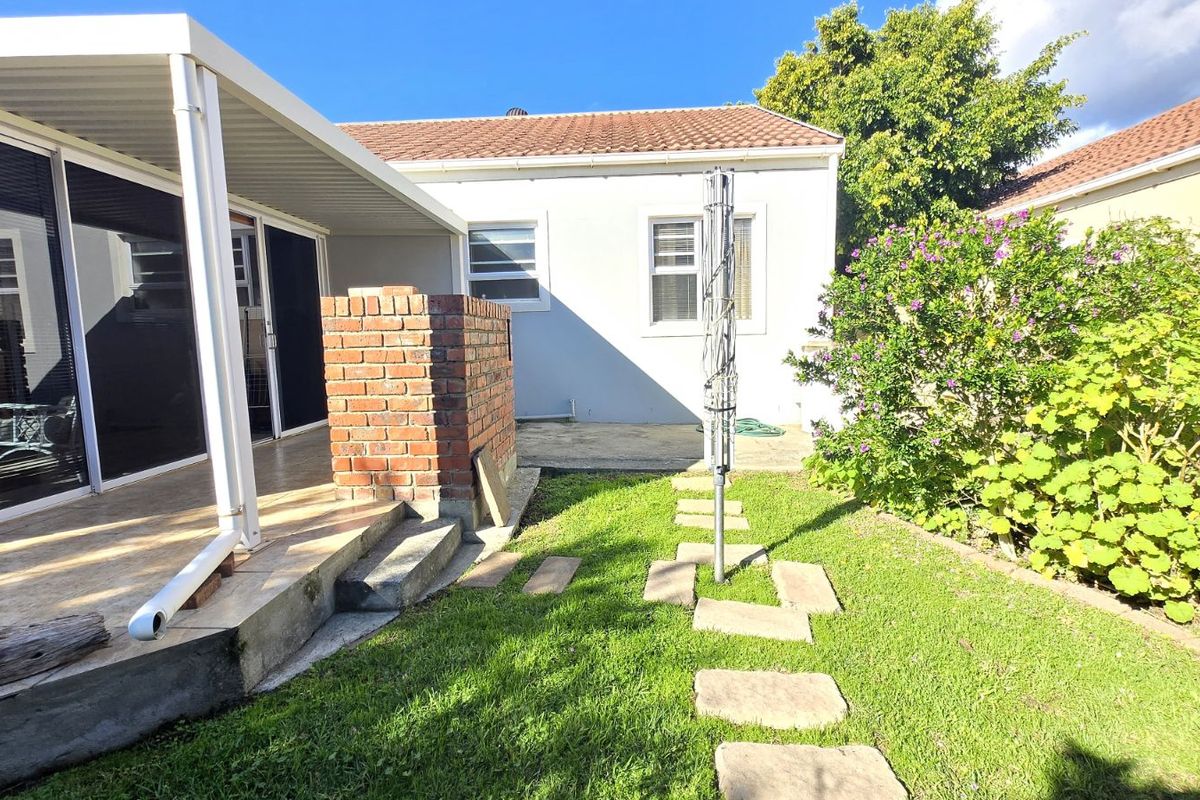 Rear exterior view featuring a covered patio with a built-in brick braai, tiled flooring, and a small garden area with stepping stones.
