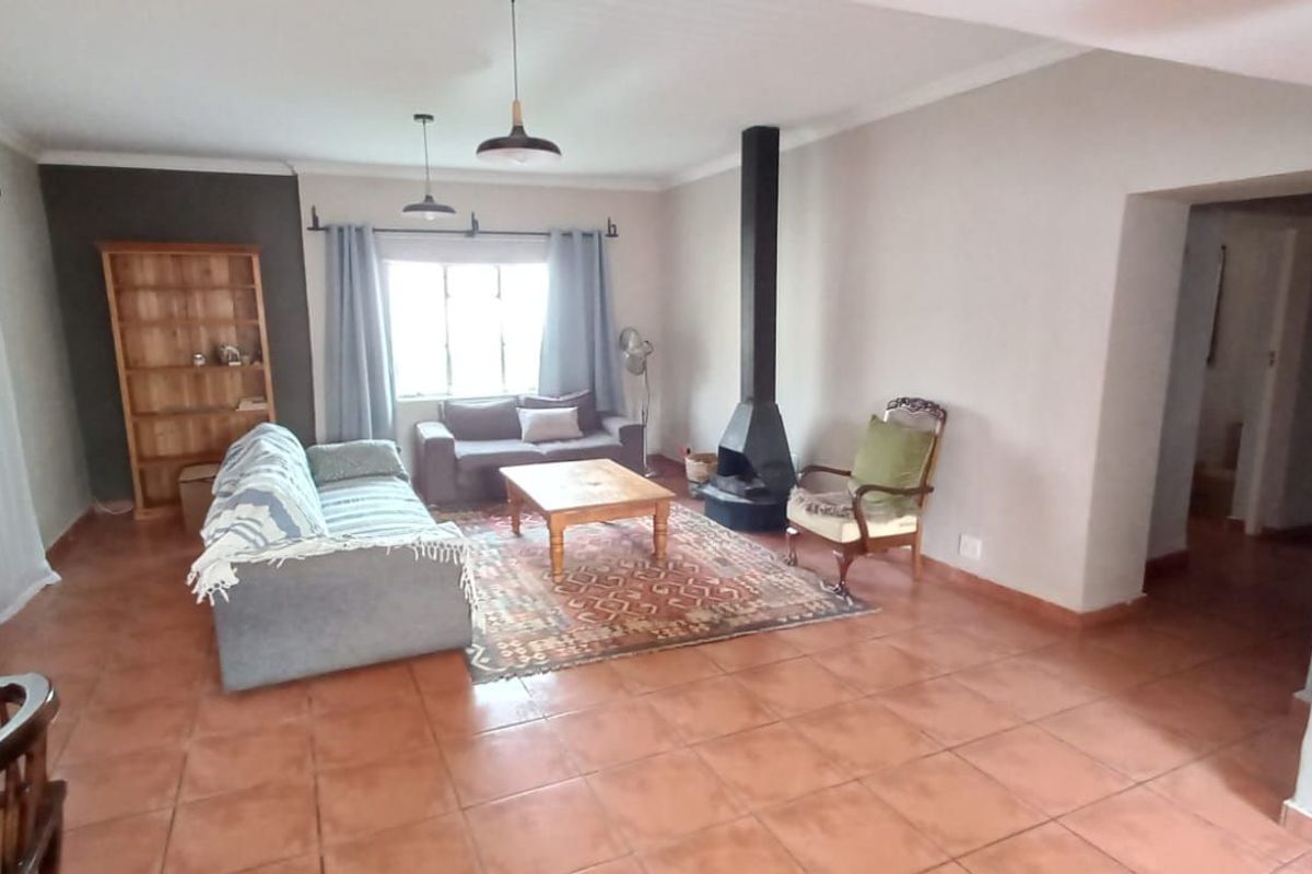 Spacious living room featuring terracotta floor tiles, a central freestanding fireplace, and large windows allowing for natural light.