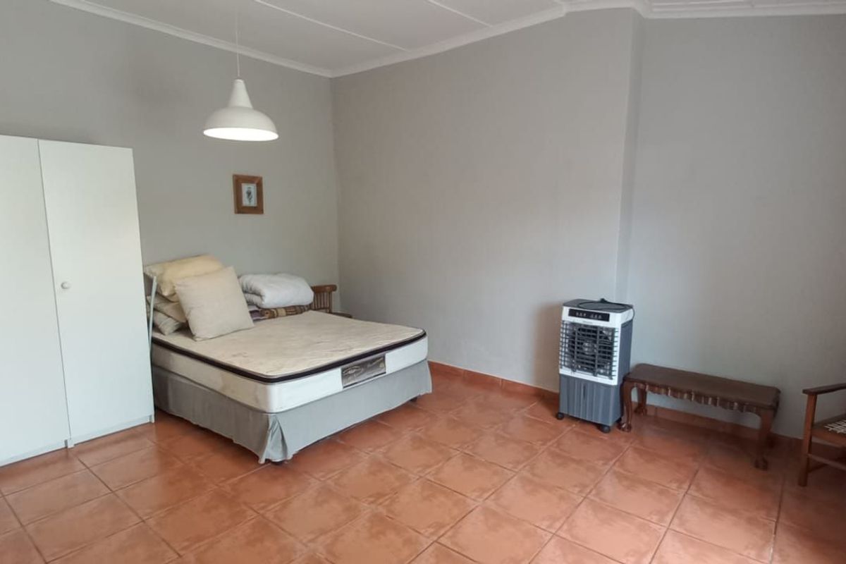 A spacious bedroom featuring tiled flooring, built-in wardrobe cabinetry, and a central pendant light fixture.