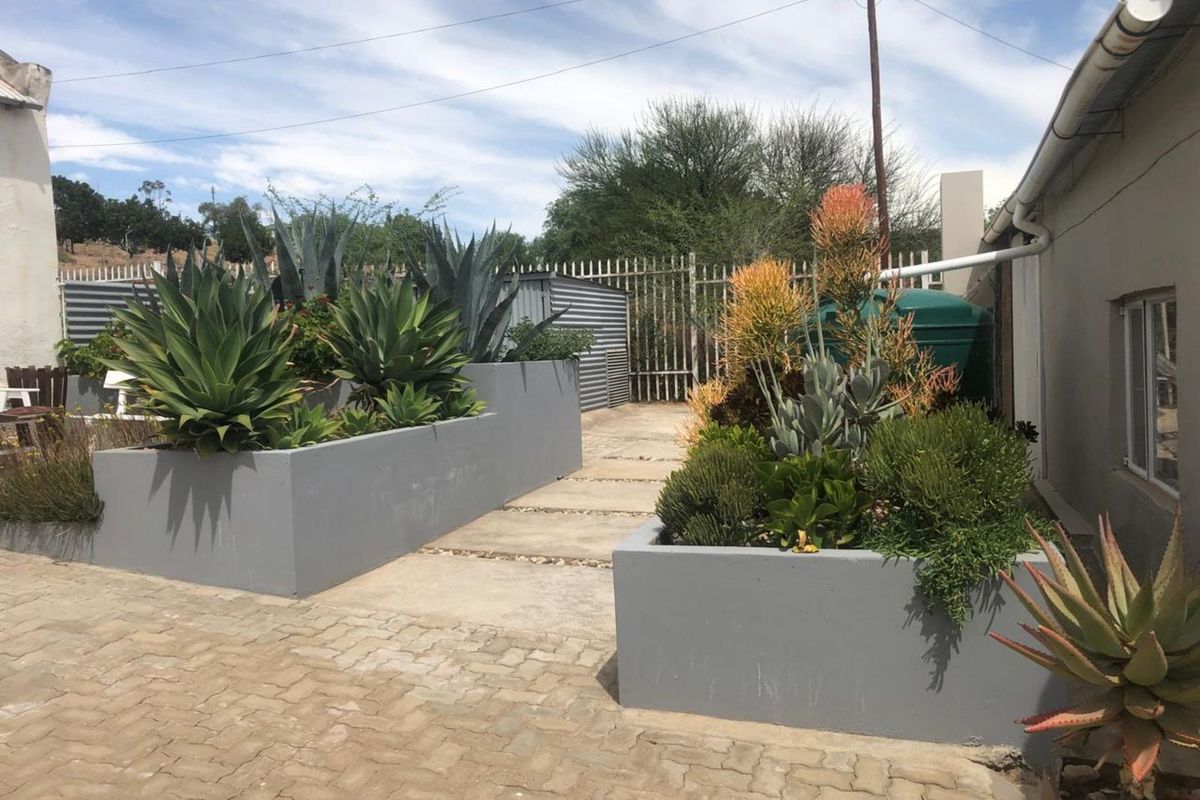 A well-maintained rear garden area featuring paved pathways, modern raised concrete planters, and a water storage tank.