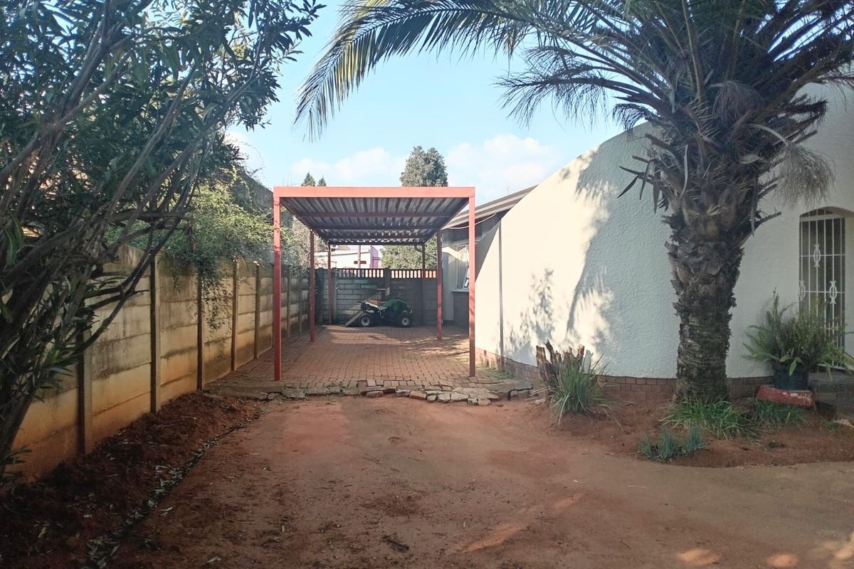 An outdoor area featuring a metal-framed carport structure, paved driveway section, and boundary walling, set alongside the side elevation of the house.