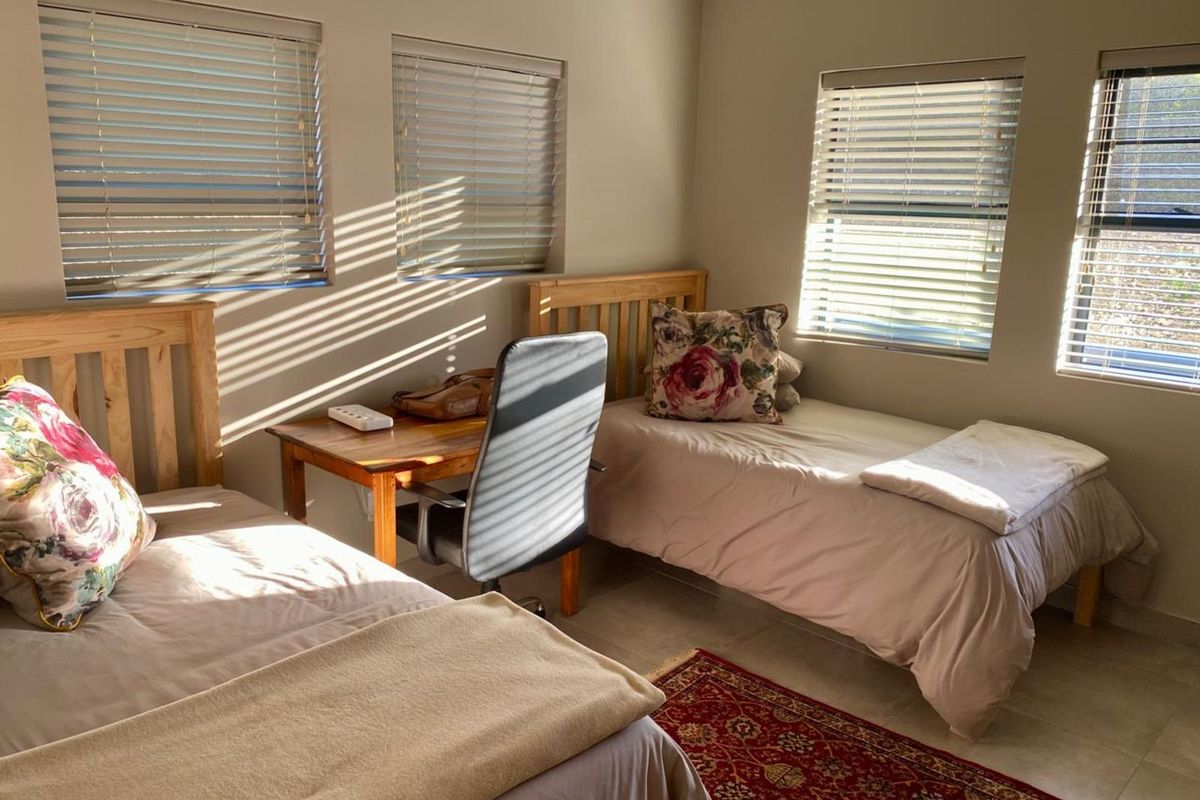 A well-lit bedroom featuring tiled flooring, neutral wall tones, and multiple windows fitted with venetian blinds.