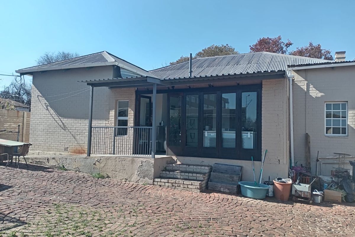Rear view of the property featuring a brick facade, corrugated metal roof, and a covered patio area with folding doors leading to the interior.