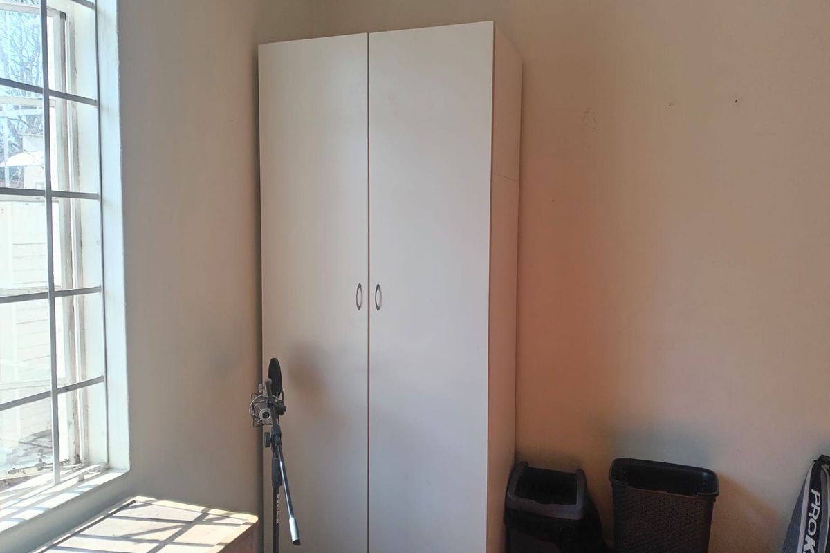 A bedroom featuring a white built-in wardrobe and a window with security bars, providing natural light and functional storage space.