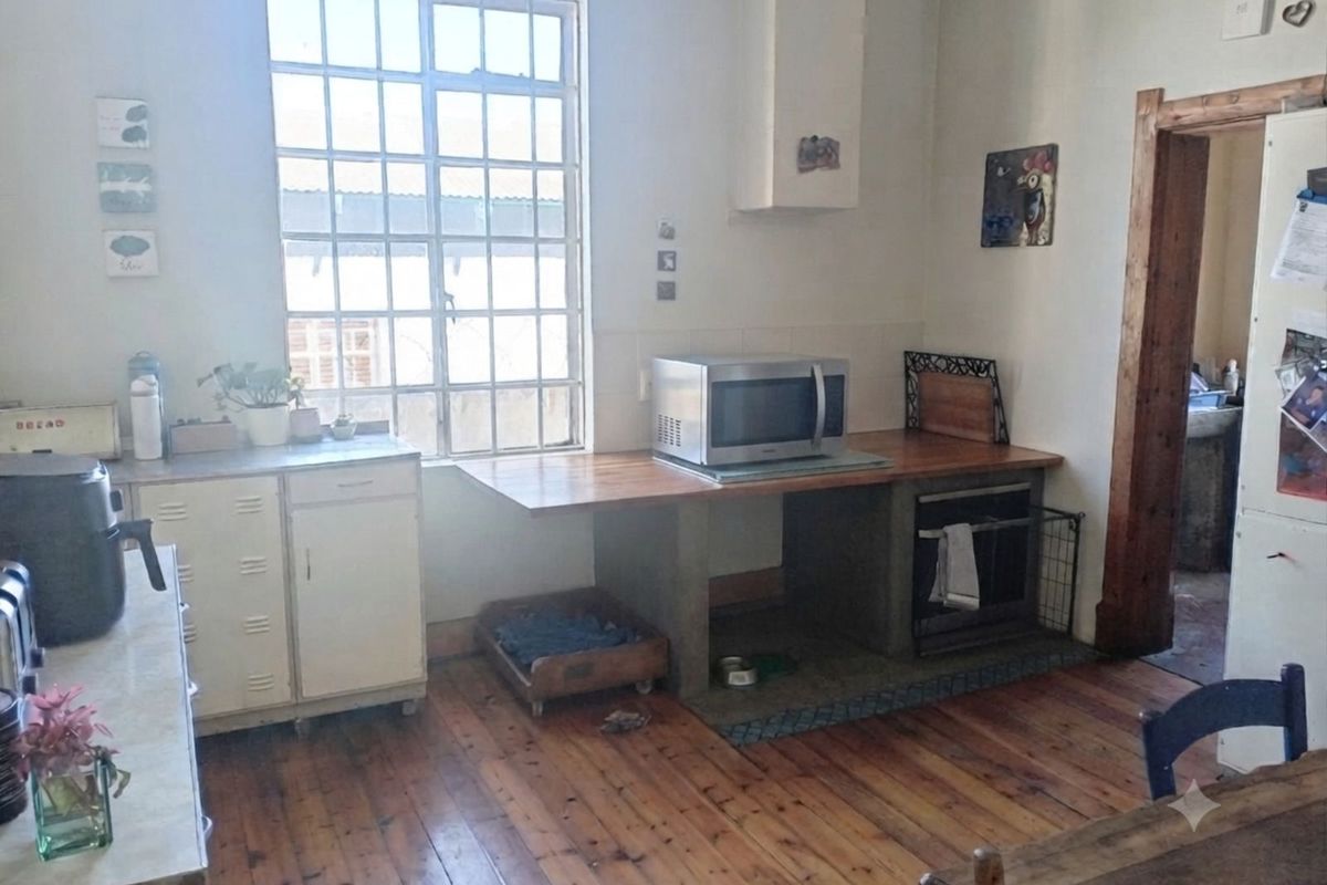 A rustic kitchen featuring timber flooring, a steel-framed window, and a concrete-based island with a timber countertop.
