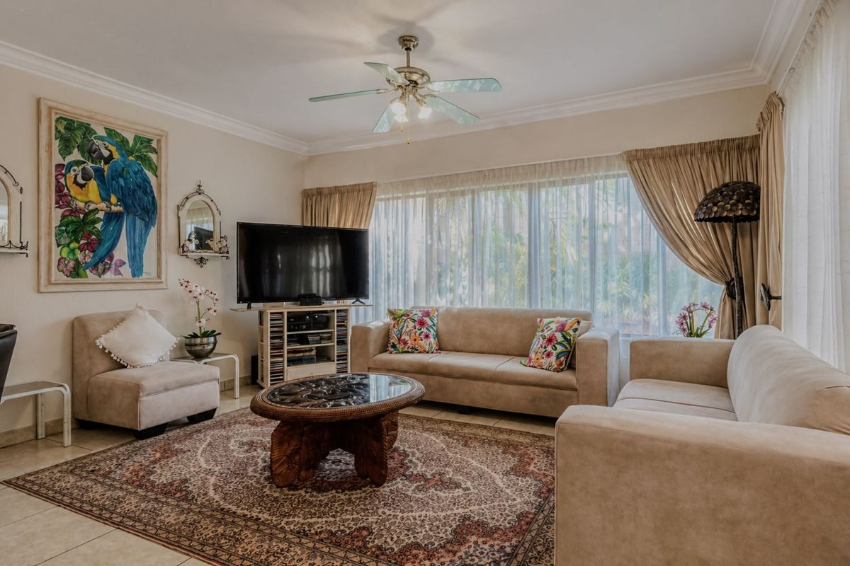 A comfortable living room featuring tiled flooring, crown molding, and a ceiling fan, with large windows providing natural light.