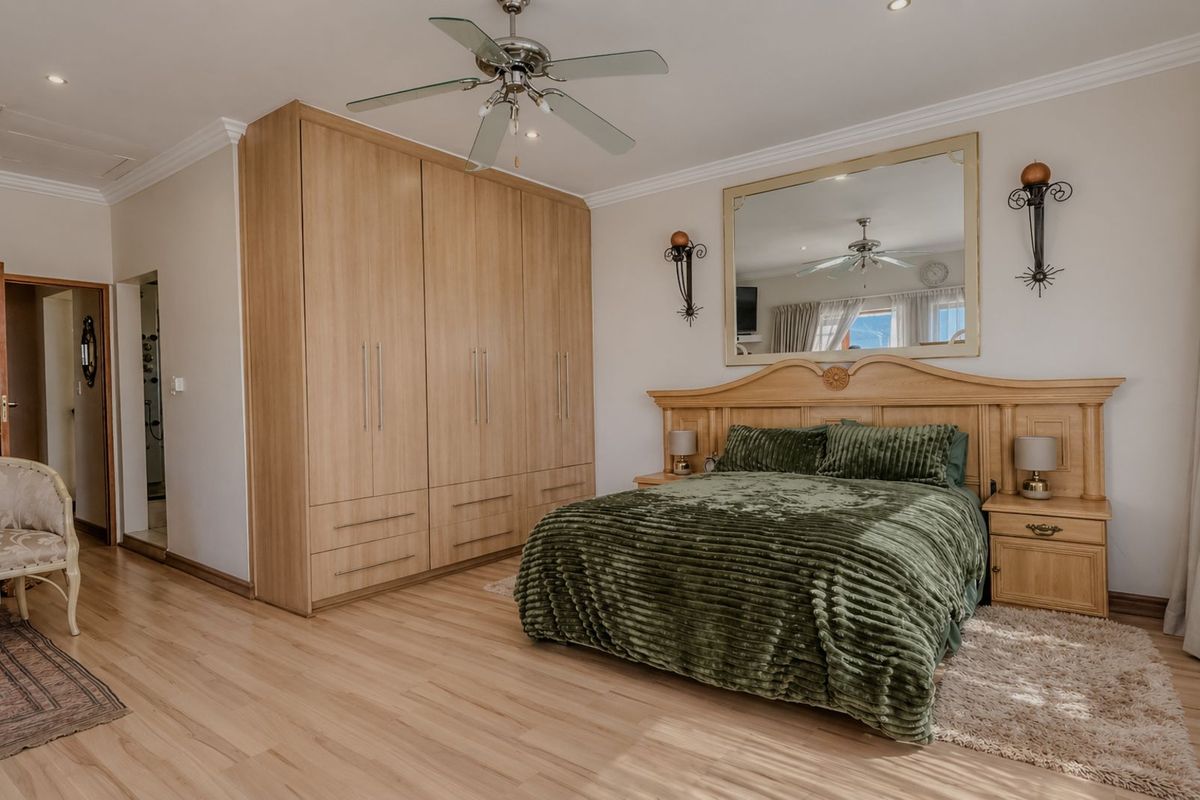 Spacious bedroom featuring light wood laminate flooring, extensive built-in cabinetry, a ceiling fan, and a large integrated headboard with matching bedside tables.