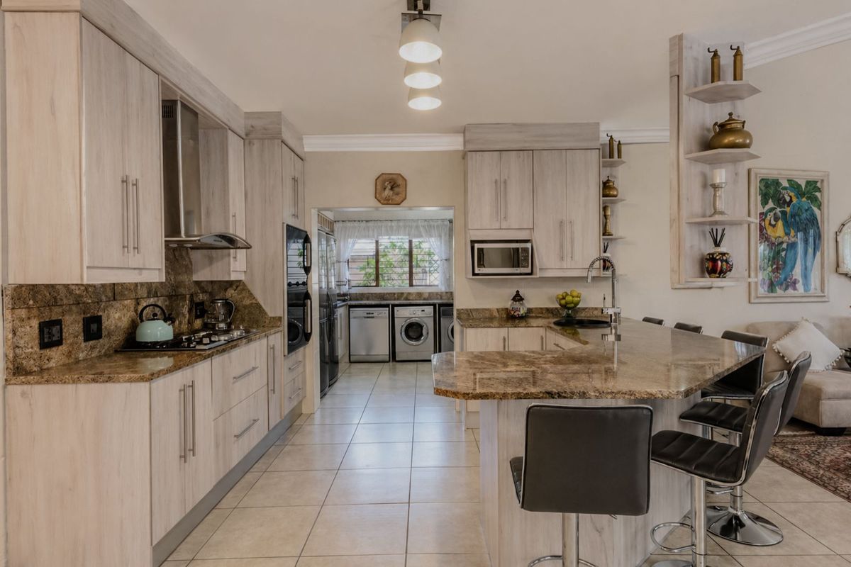 A well-appointed kitchen featuring light wood cabinetry, granite countertops, a breakfast bar, and an integrated oven, with an adjacent laundry area visible.