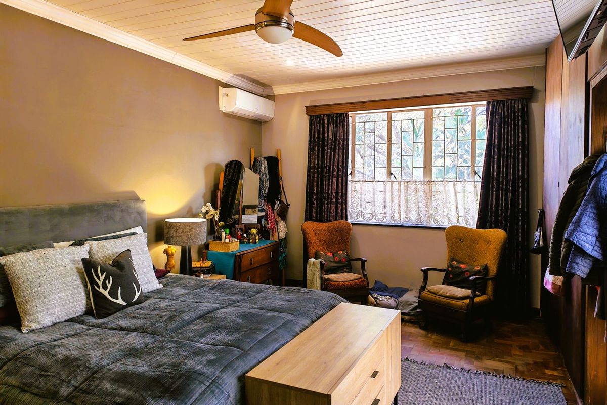 A cozy bedroom featuring parquet flooring, a timber-paneled ceiling with a central fan, and built-in wooden cabinetry.