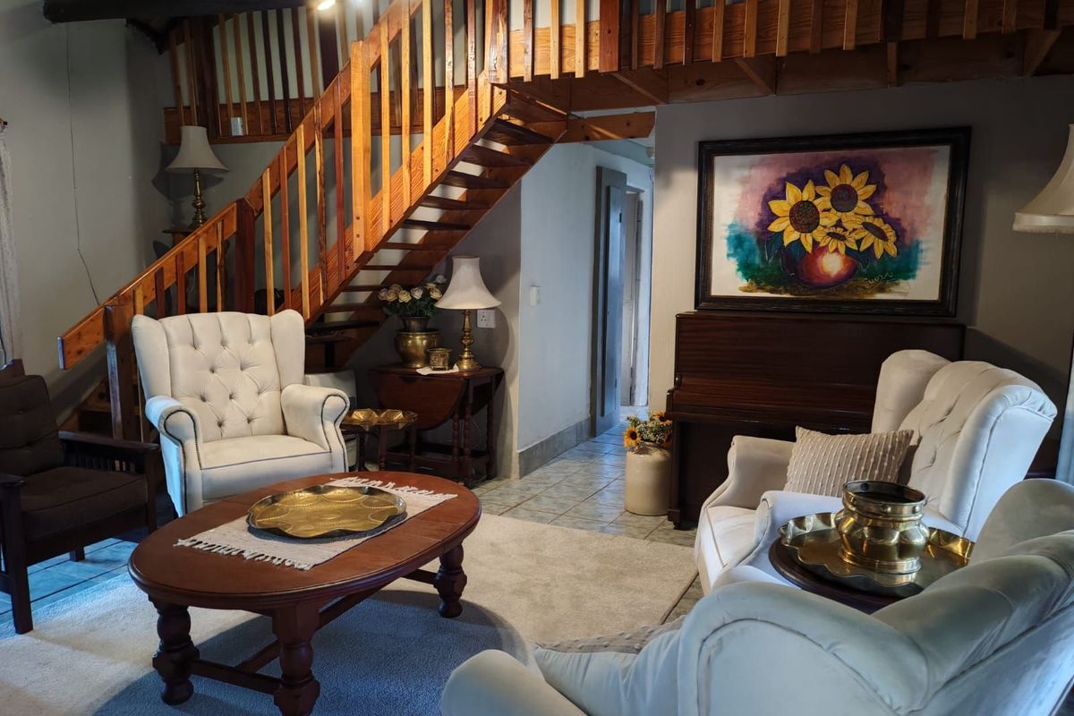 A cozy living room featuring a wooden staircase leading to a mezzanine level, tiled flooring, and a traditional interior layout.