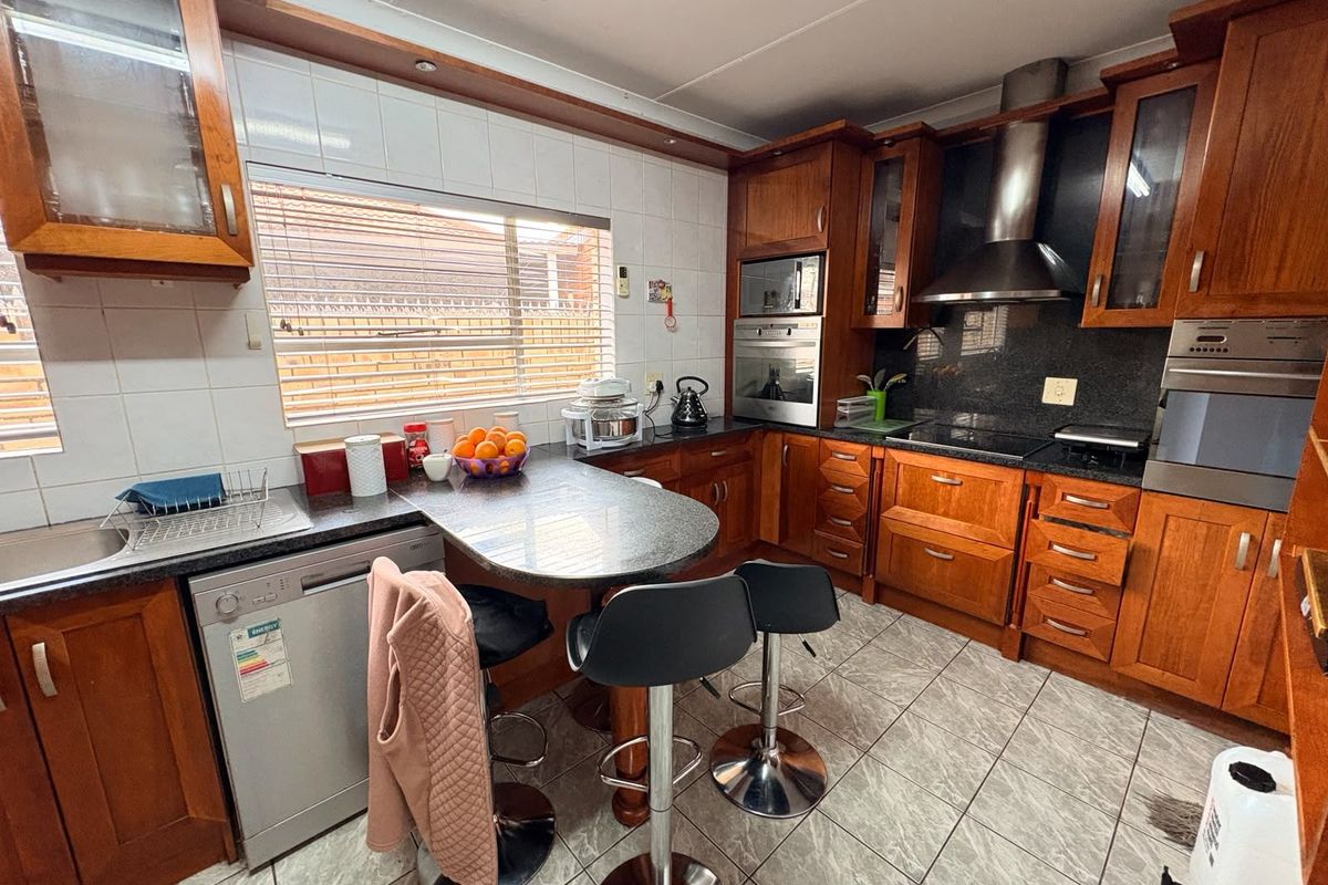 A functional kitchen featuring timber cabinetry, granite-style countertops, a built-in oven, extractor fan, and a breakfast nook with tiled flooring.