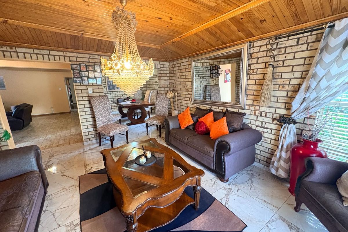 A living room featuring exposed brick walls, a timber-clad vaulted ceiling, and polished floor tiles, illuminated by a large decorative crystal chandelier.