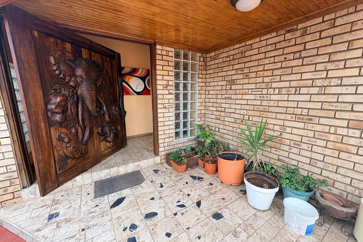 Covered entrance porch featuring a decorative carved wooden door, face brick walls, glass block accents, and tiled flooring.