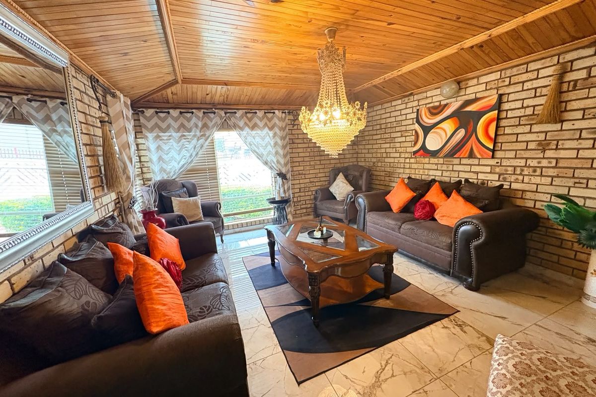A living room featuring exposed brick walls, a vaulted timber-clad ceiling, and polished marble-look floor tiles.