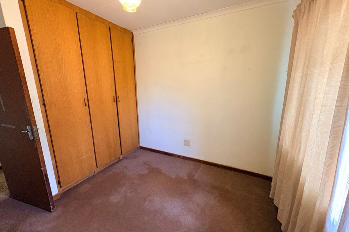 A bedroom featuring built-in wooden cupboards, carpeted flooring, and a standard light fixture, presenting a dated interior in need of cosmetic updates.