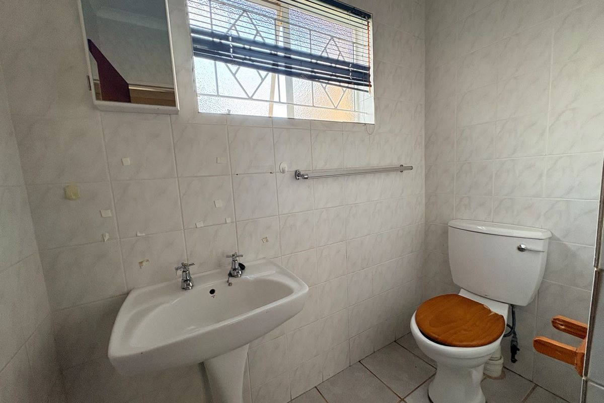 A functional bathroom featuring a pedestal basin, toilet, and tiled walls. The space requires cosmetic updates to address tile damage and general wear.