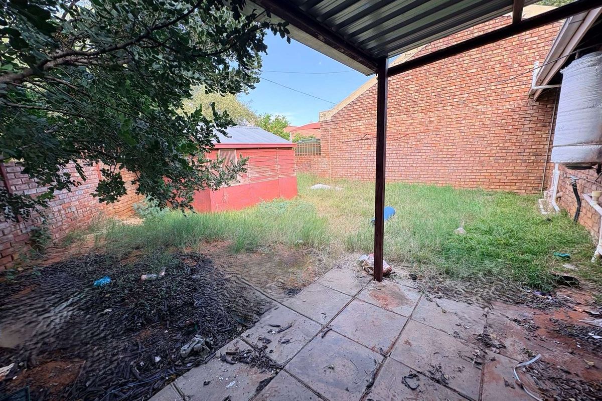 A rear garden area featuring a covered patio, brick boundary walls, and an existing storage shed, requiring significant landscaping and maintenance.