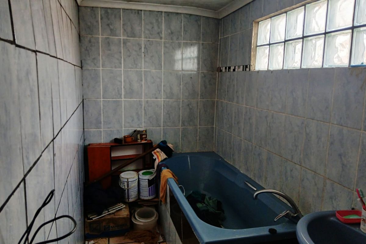 A dated bathroom featuring blue sanitary ware, tiled walls, and a glass block window, requiring modernization and cosmetic updates.