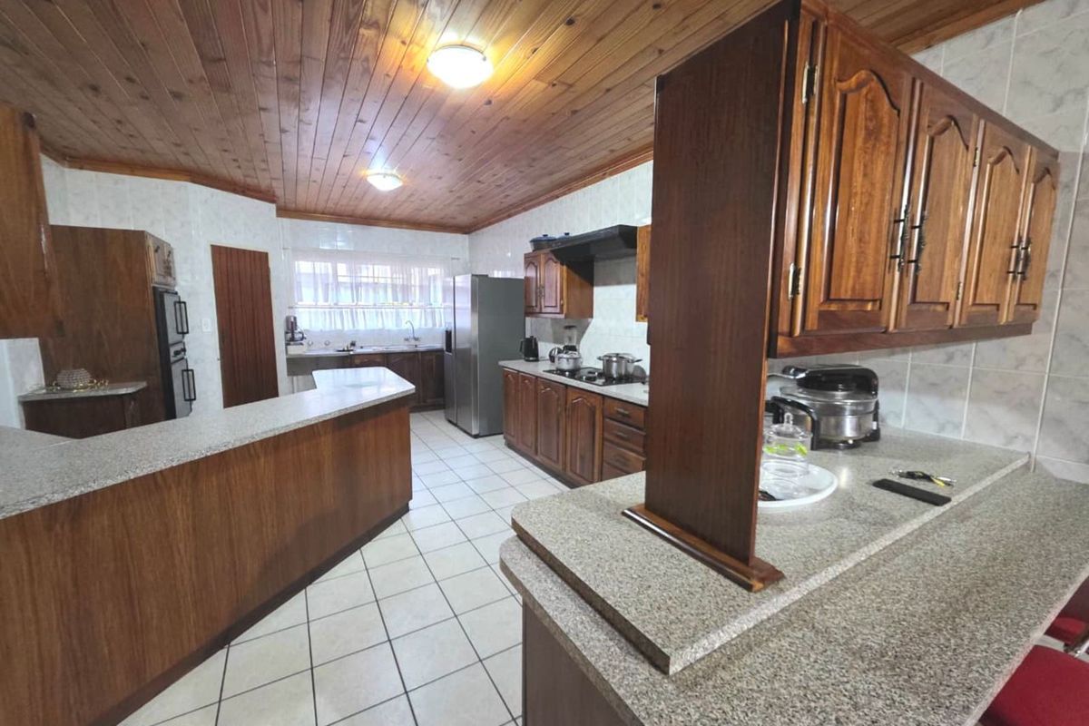 Spacious kitchen featuring timber cabinetry, granite-look countertops, tiled flooring, and a distinctive timber-clad ceiling with integrated lighting.