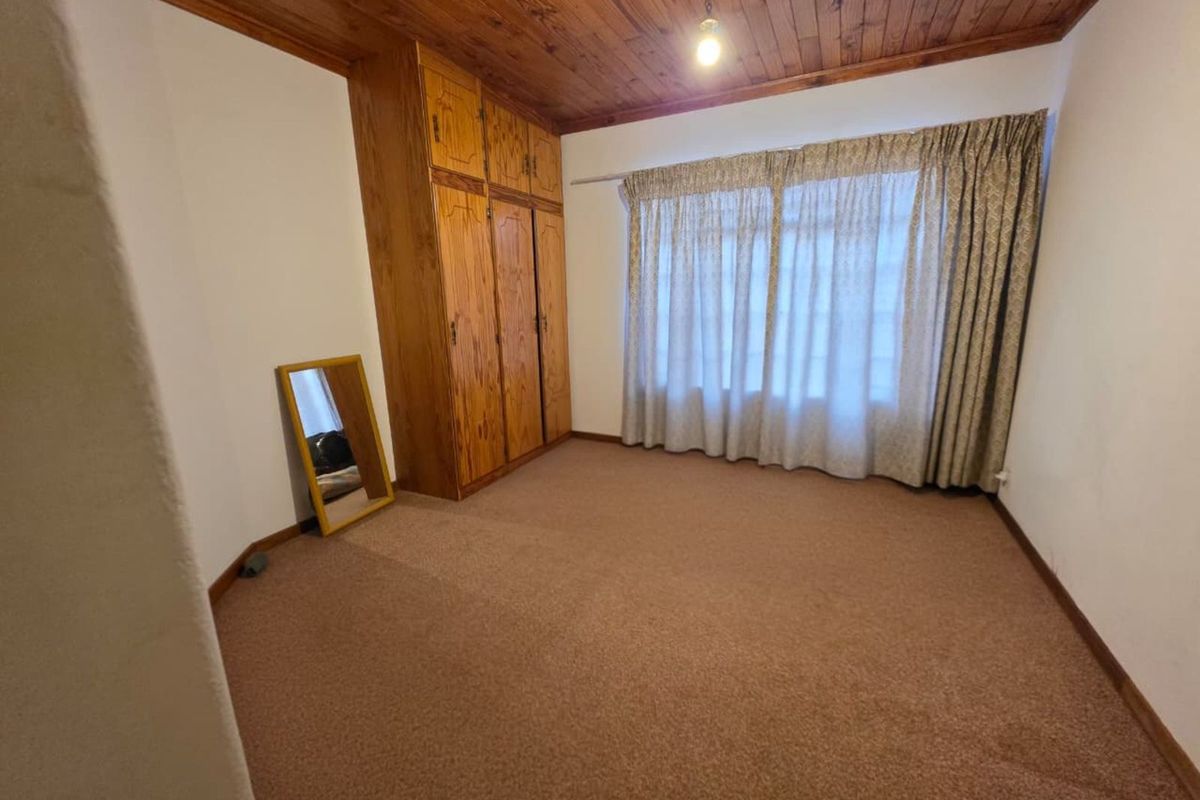 A bedroom featuring a timber-paneled ceiling, built-in wooden cupboards, and carpeted flooring, offering a dated aesthetic ready for modernization.
