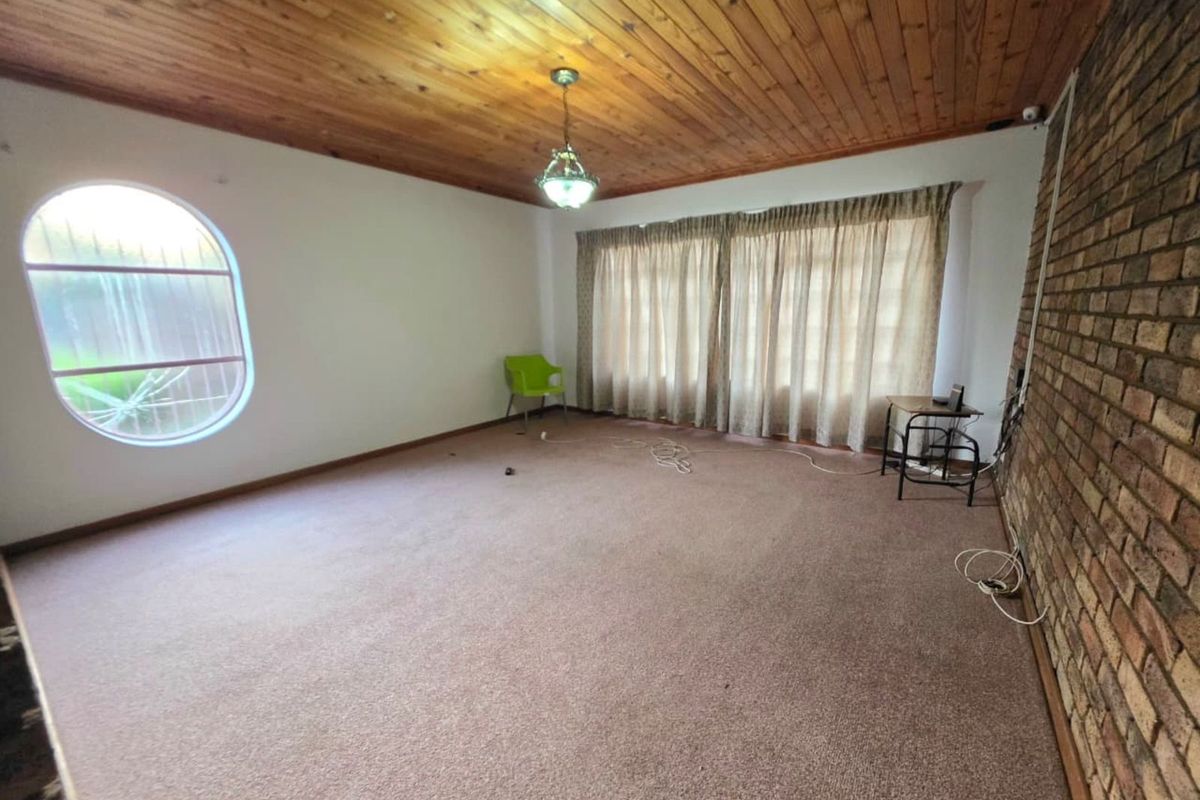 Spacious living room featuring a distinctive circular window, exposed brick feature wall, and timber-paneled ceiling, offering a versatile layout for comfortable family living.