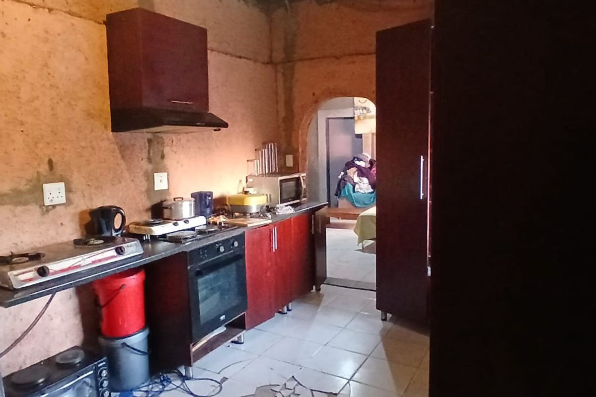 A compact kitchen featuring dark wood cabinetry, a built-in oven, and an extractor fan, requiring significant cosmetic renovation and wall repairs.